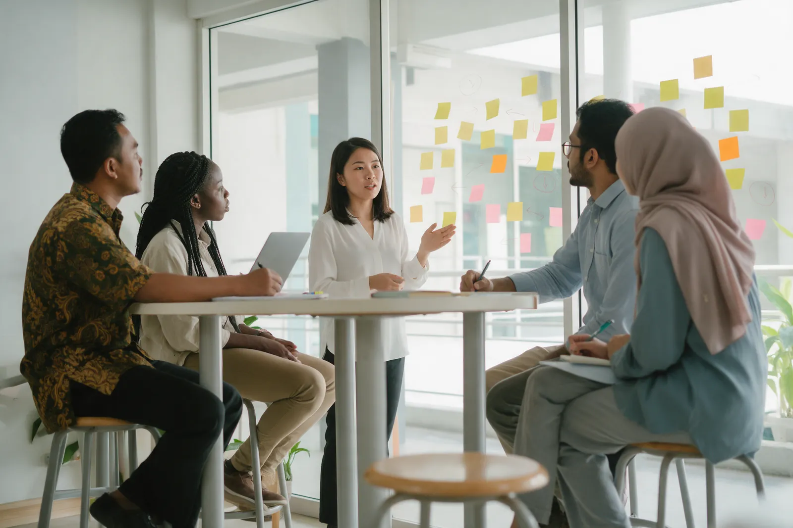A student presenting to classmates in front of a glass wall covered in coloured sticky notes