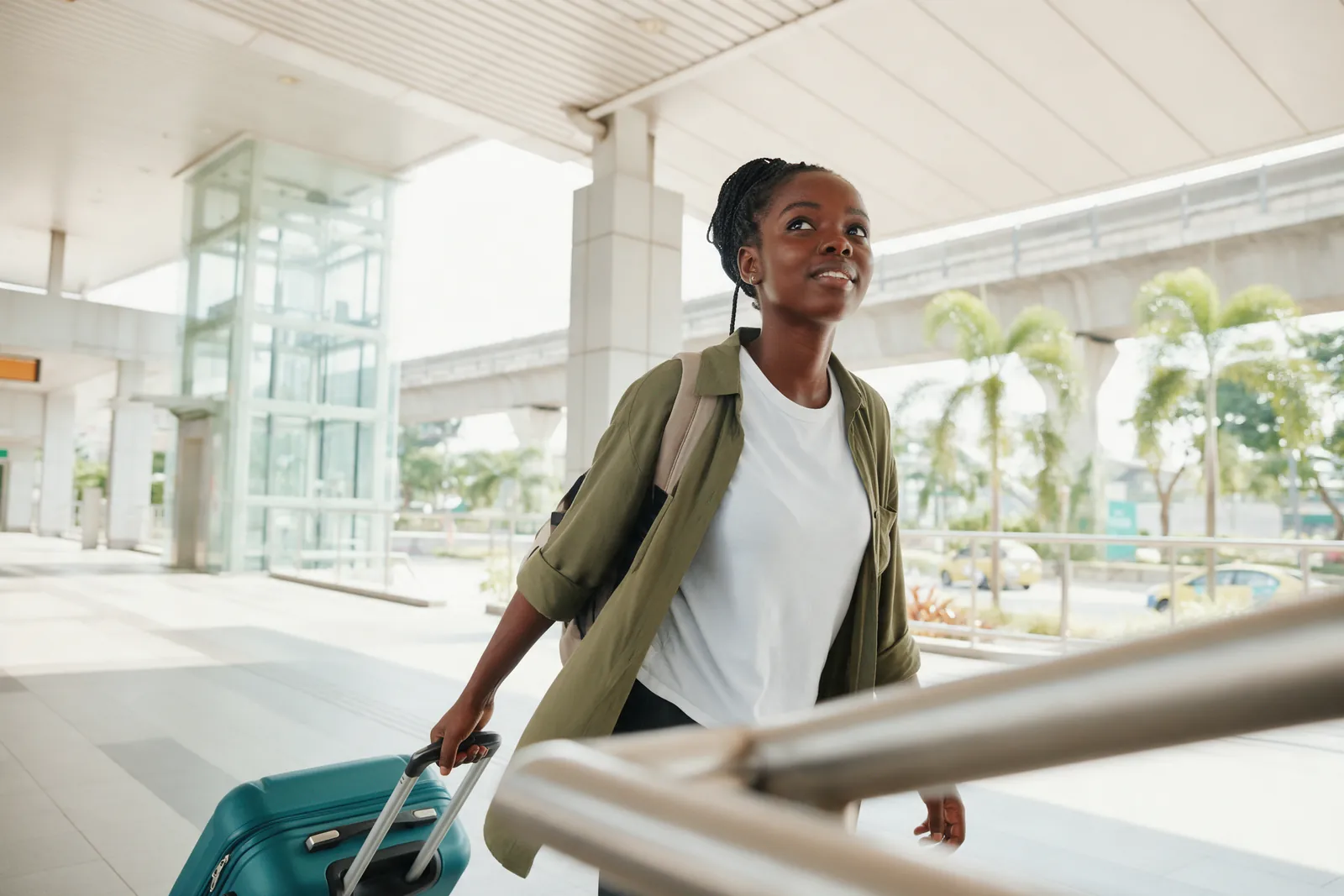 An international student with a suitcase and backpack on a sunlit walkway with city towers behind